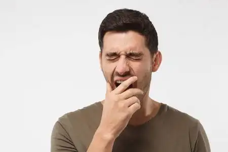 无聊的年轻人打呵欠沉睡的年轻人打呵欠, 醒来, 用手闭上嘴巴, 在灰色